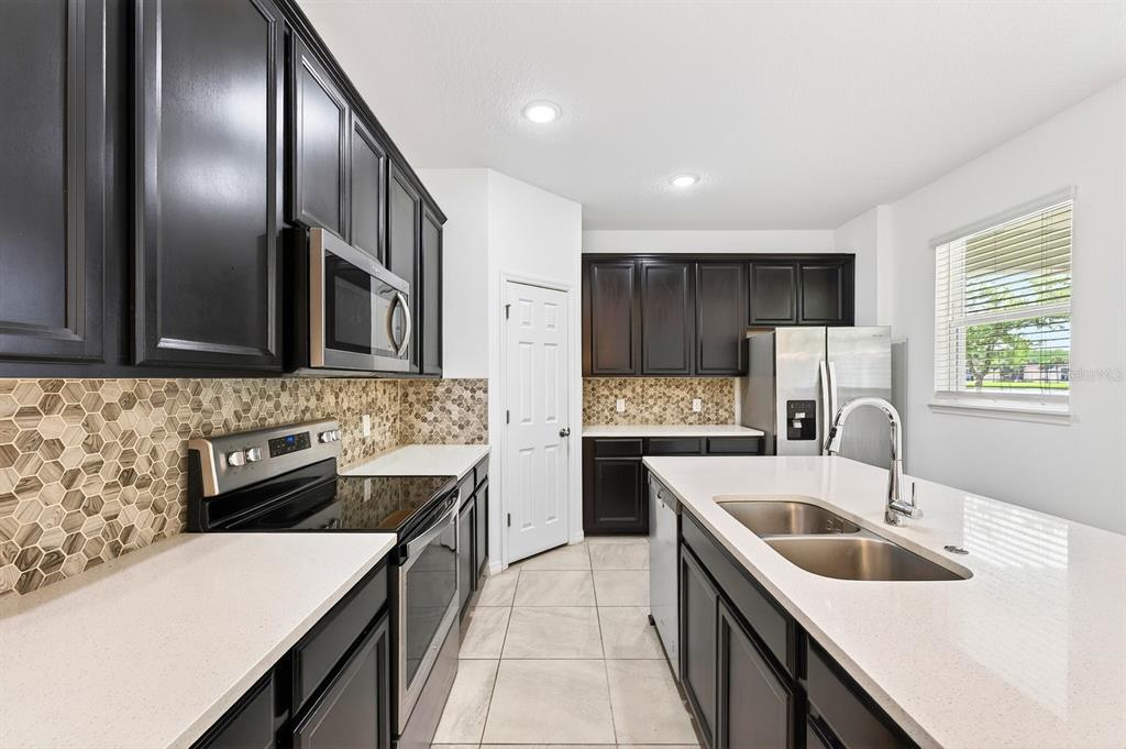 A kitchen features dark wood cabinets, white countertops, stainless steel appliances, and a hexagonal backsplash — 15523 WILLOW ARBOR CIRCLE, ORLANDO, FL