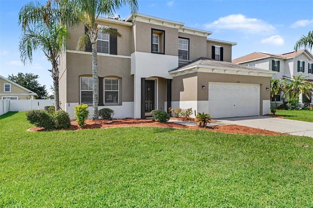 A two-story suburban house with a tan stucco exterior, a white garage, and palm trees — 2012 BEARING LANE, KISSIMMEE, FL