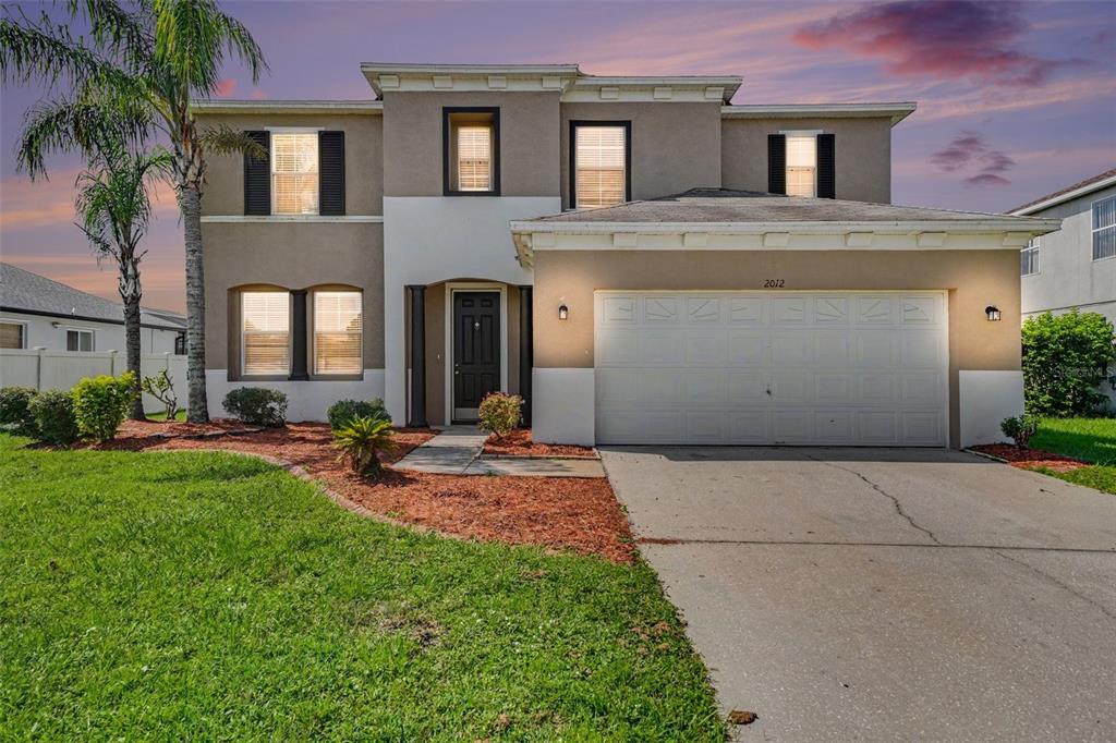 A two-story suburban house with a beige stucco exterior, a two-car garage, and a palm tree — 2012 BEARING LANE, KISSIMMEE, FL