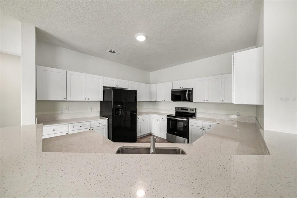 An open-concept living and dining area features wood-look flooring, tile in the kitchen, and white walls — 2012 BEARING LANE, KISSIMMEE, FL