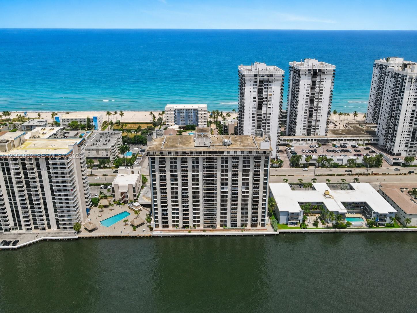 An aerial view shows several high-rise apartment buildings situated between a waterway and the ocean — 1600 S Ocean Dr # 18B, Hollywood FL 33019, HOLLYWOOD, FL