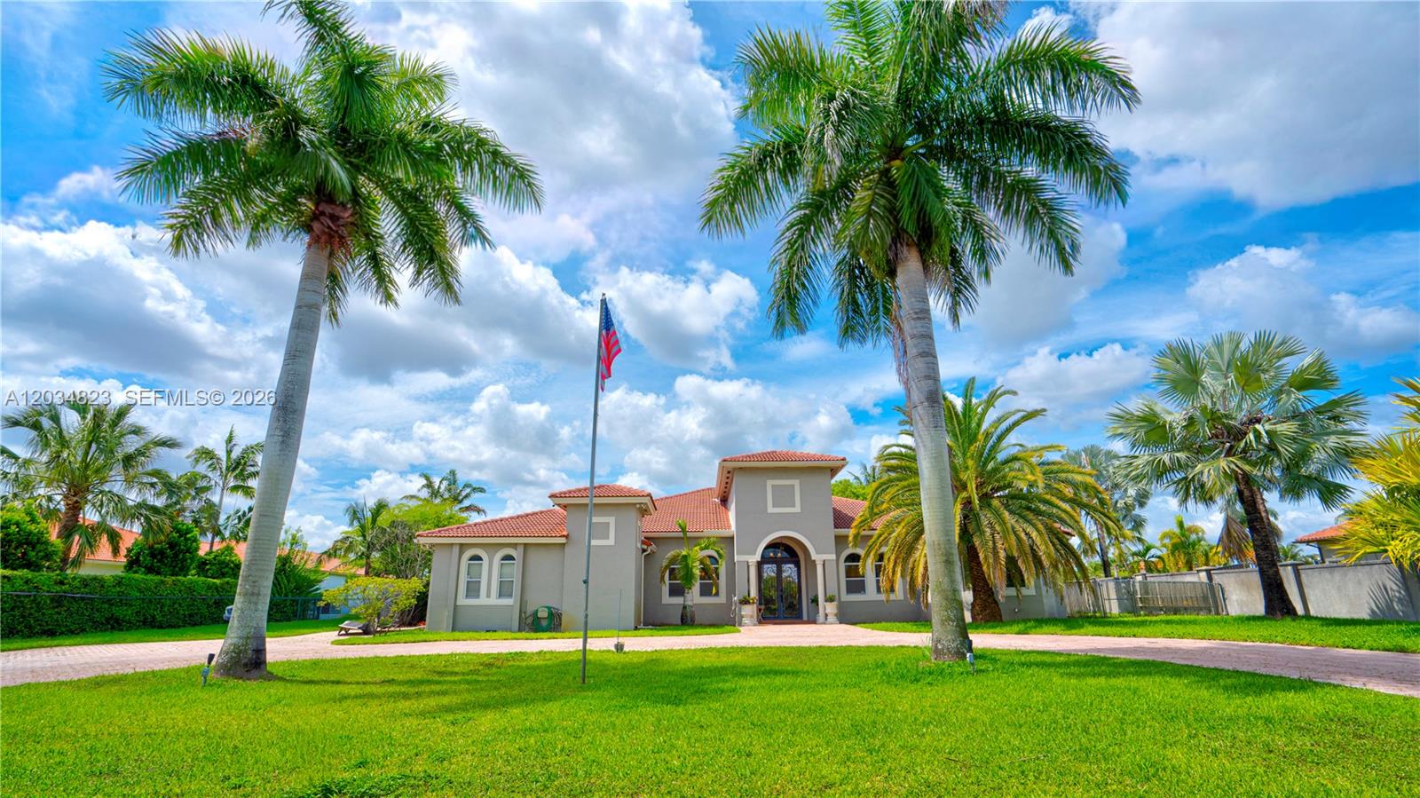 A single-story house with a tile roof and palm trees sits on a grassy lawn — 9810 NW 137th St, Hialeah Gardens FL 33018, HIALEAH GARDENS, FL