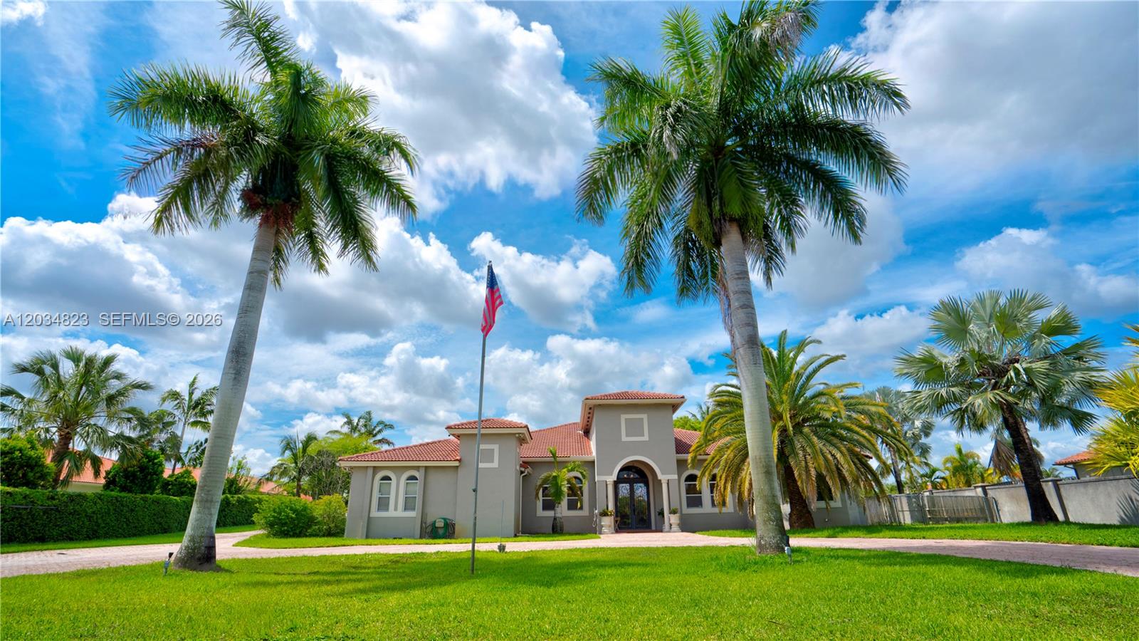 A single-story house with a tiled roof sits behind a lawn with tall palm trees — 9810 NW 137th St, Hialeah Gardens FL 33018, HIALEAH GARDENS, FL