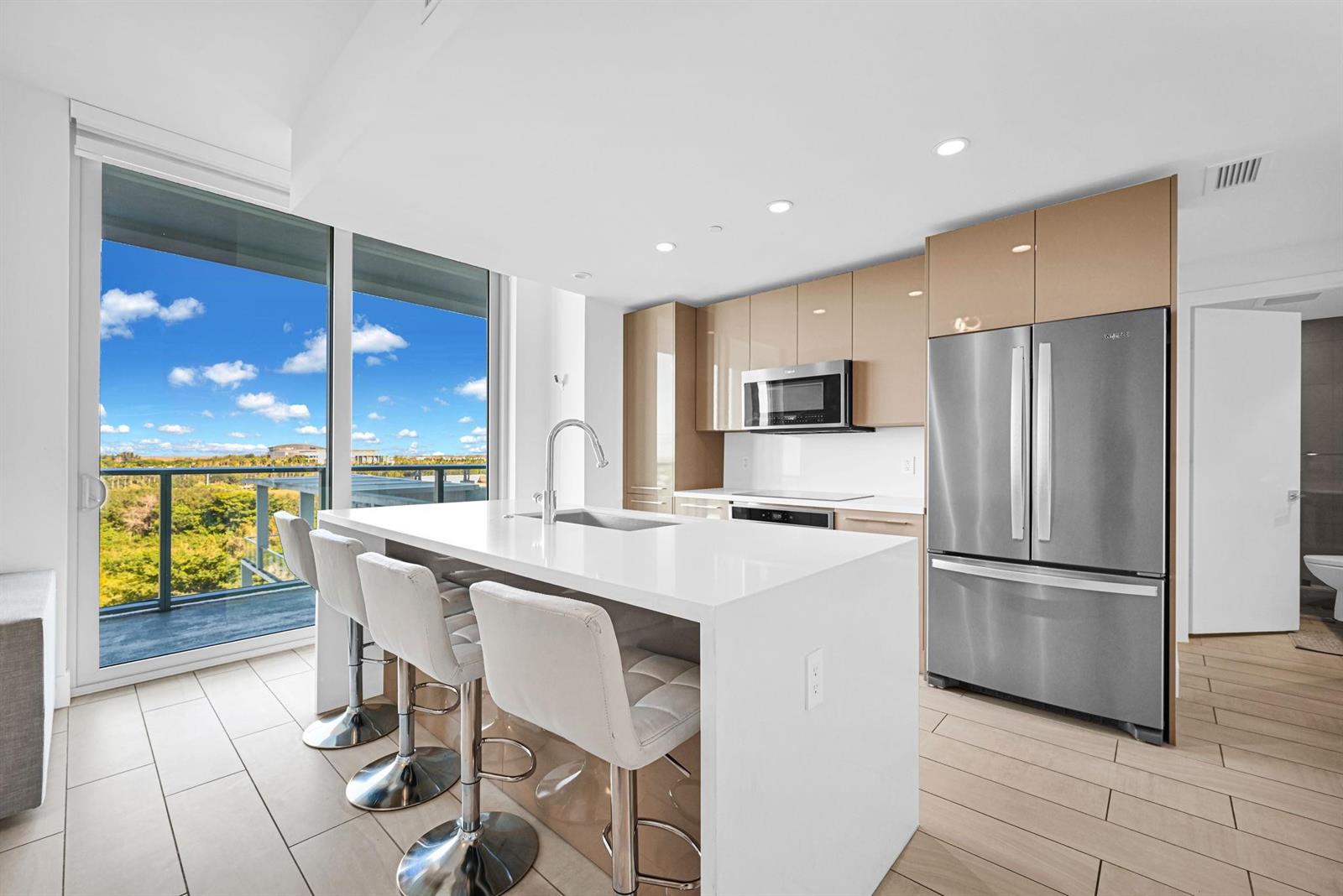 A modern kitchen features a white island, stainless steel appliances, and a balcony with views — 2000 Metropica Way # 801, Sunrise FL 33323, SUNRISE, FL
