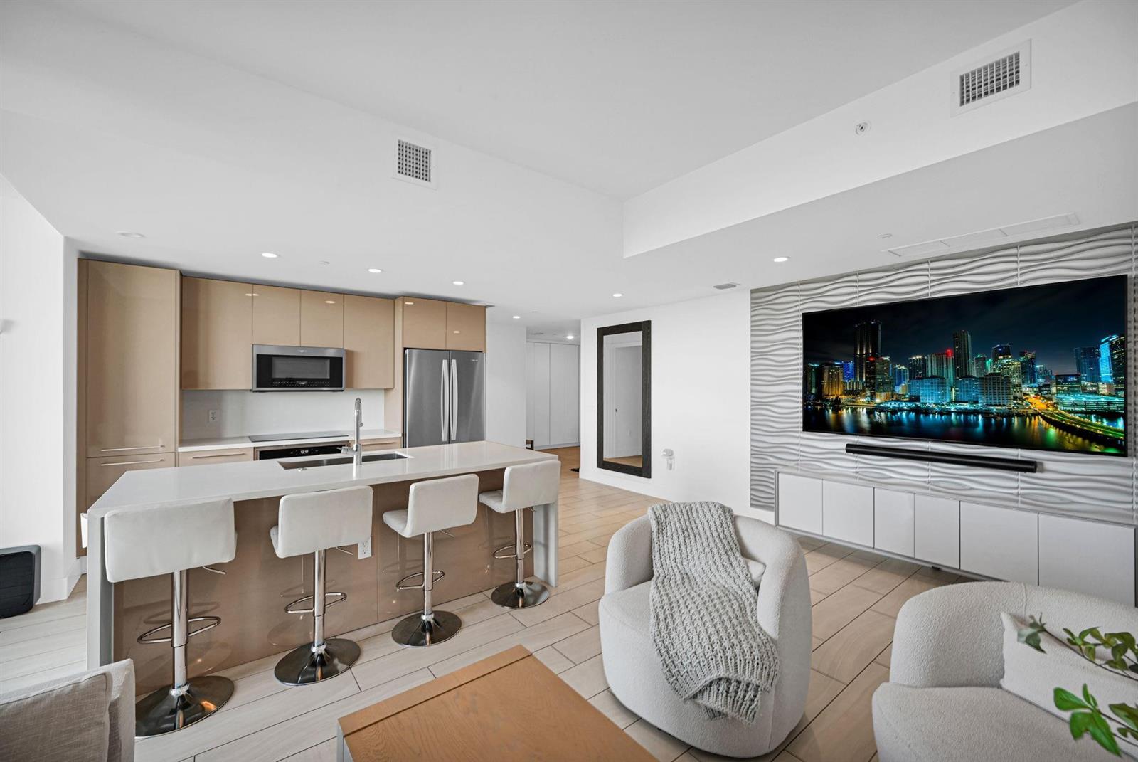 A modern open-concept kitchen and living area features light wood cabinetry and a textured wall — 2000 Metropica Way # 801, Sunrise FL 33323, SUNRISE, FL