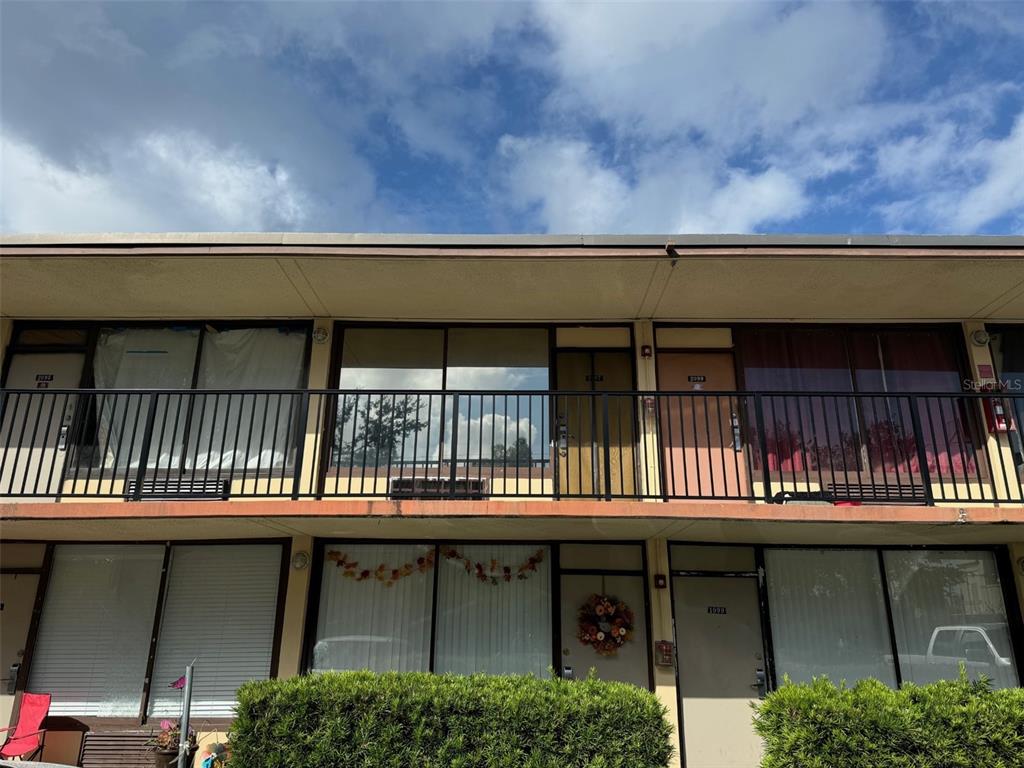 A two-story apartment building exterior features a balcony with black railings and ground-floor entry doors — 7900 S ORANGE BLOSSOM TRAIL UNIT 2097, ORLANDO, FL