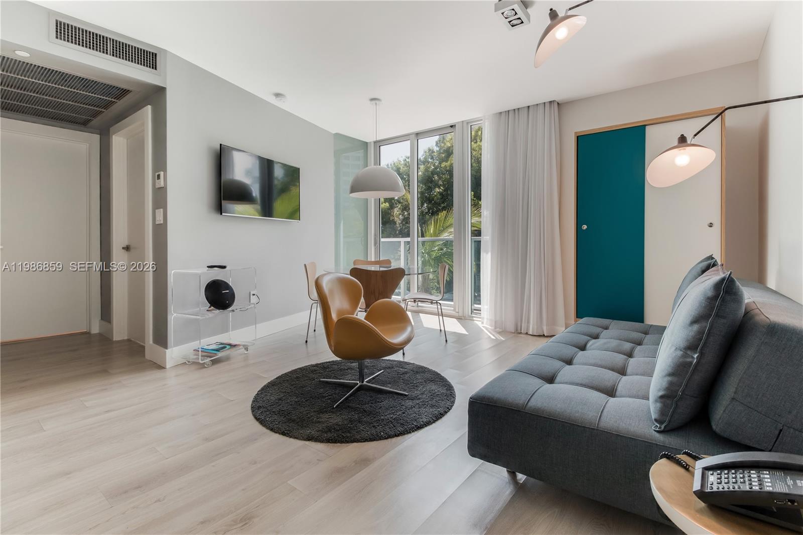 A modern living room features a gray sofa, a tan accent chair, and floor-to-ceiling windows — 1215 West Ave # 402, Miami Beach FL 33139, MIAMI BEACH, FL