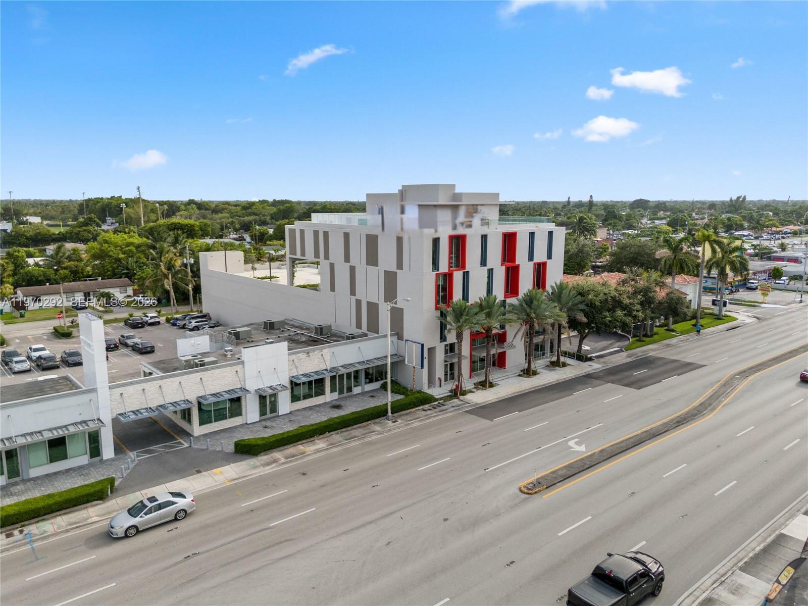 An aerial view shows a modern multi-story building with red accents next to a parking lot — 8966 Bird Road, Miami FL 33165, MIAMI, FL