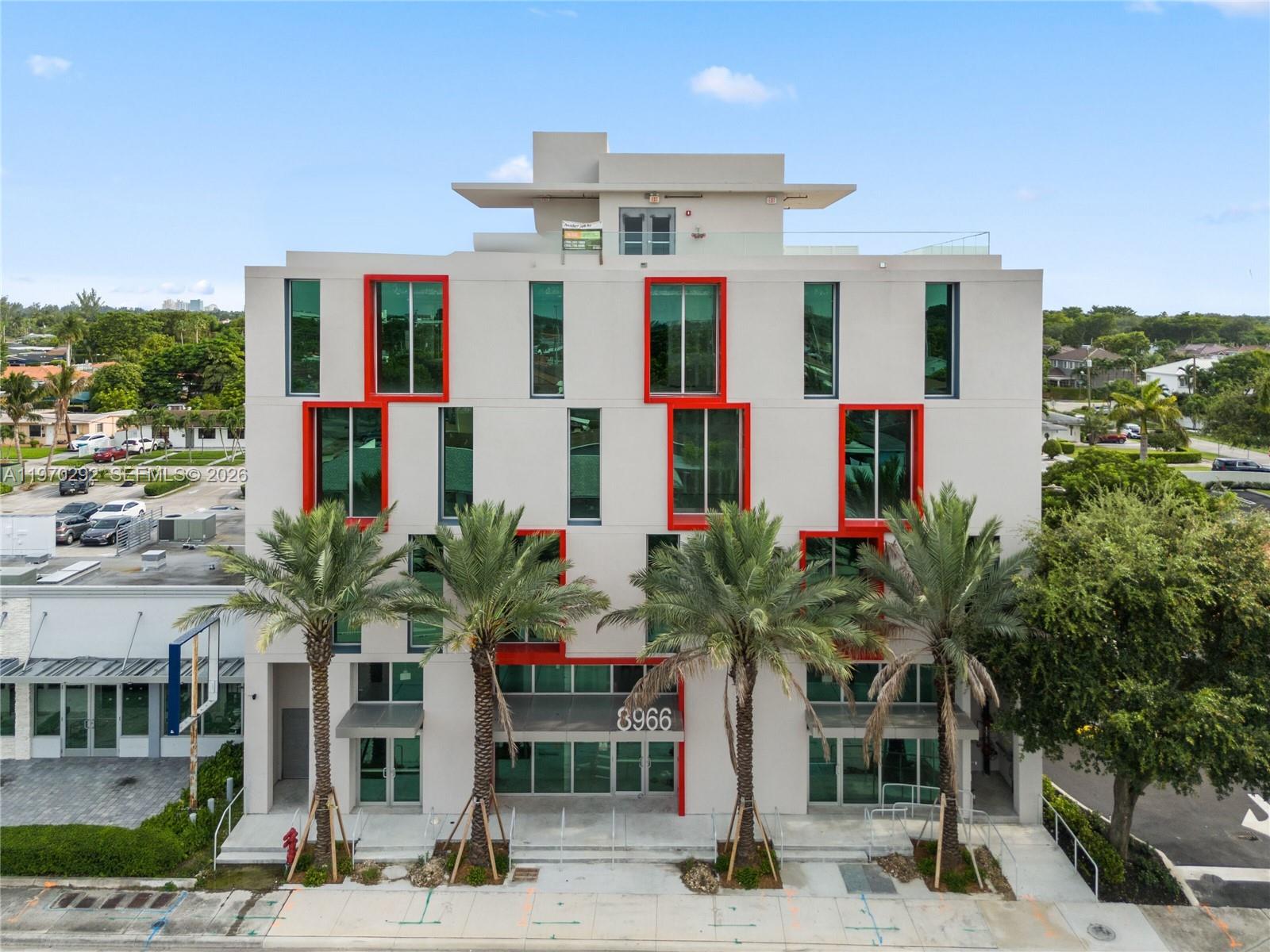 A modern four-story building features a white facade with prominent red-framed windows and palm trees — 8966 Bird Road, Miami FL 33165, MIAMI, FL