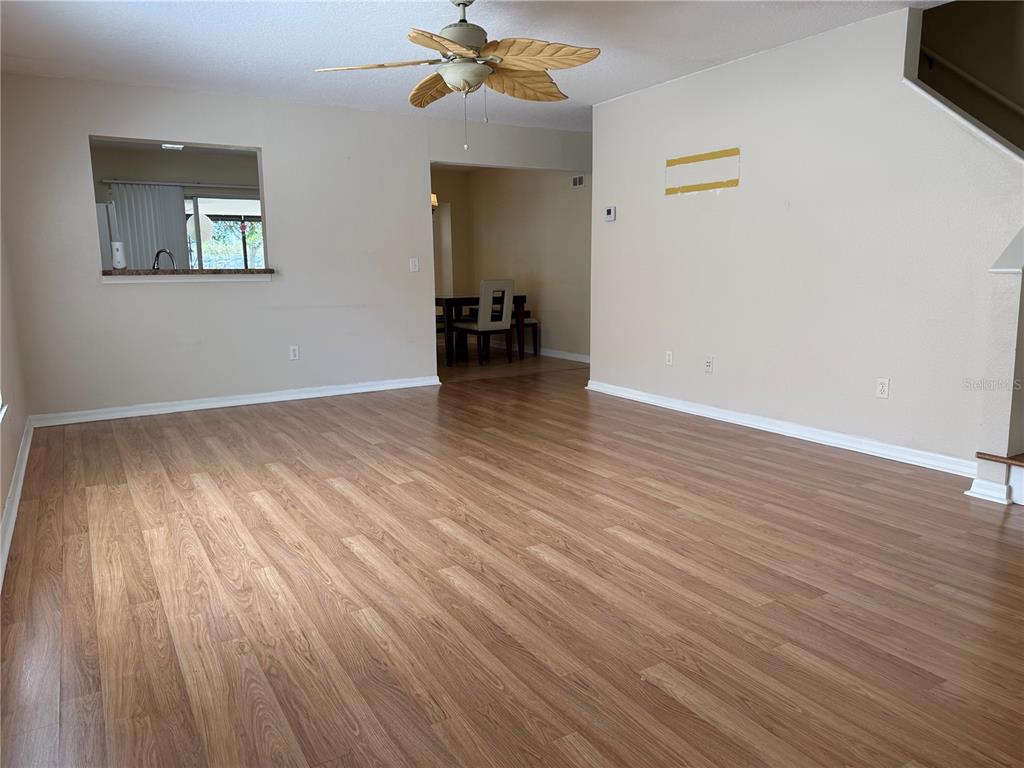 An empty living room features light wood-look flooring, beige walls, and a ceiling fan — 5901 WRENWATER DRIVE, LITHIA, FL