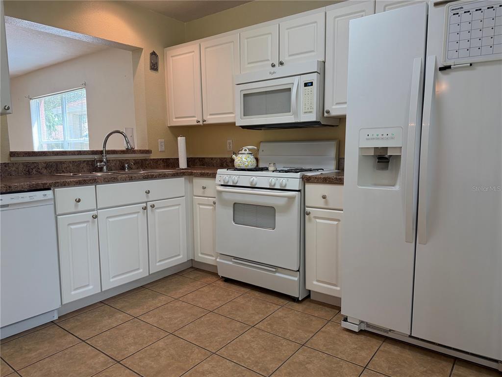 A kitchen features white cabinets, white appliances, brown countertops, and brown tile flooring — 5901 WRENWATER DRIVE, LITHIA, FL