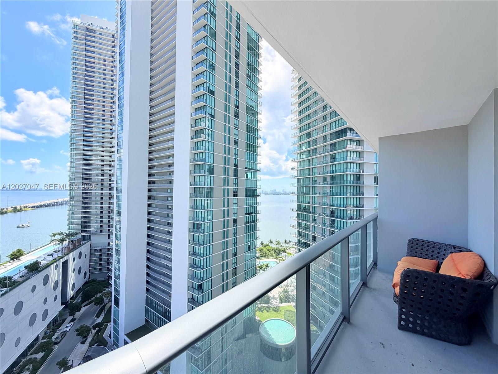 A balcony with a wicker chair overlooks high-rise buildings and a bay — 501 NE 31st St # 1804, Miami FL 33137, MIAMI, FL