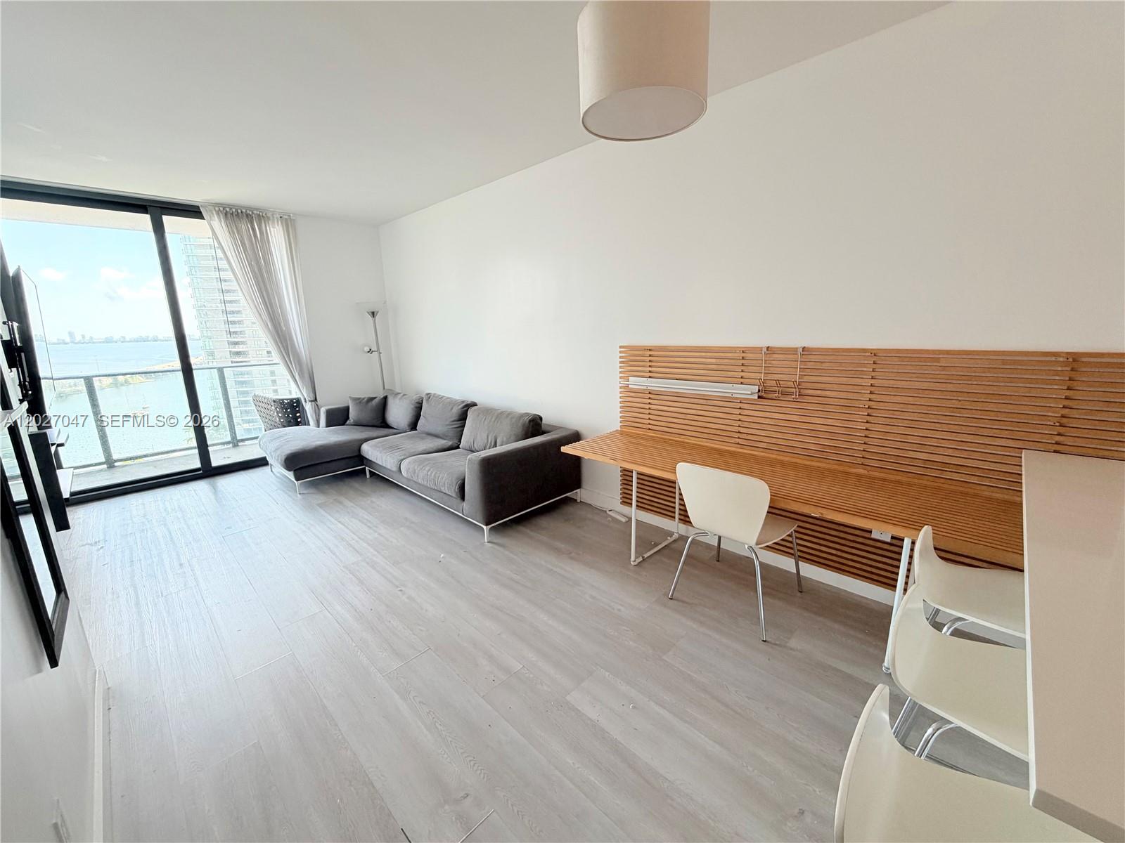 A living room features a gray sectional sofa, a wooden wall-mounted desk, and a balcony view — 501 NE 31st St # 1804, Miami FL 33137, MIAMI, FL