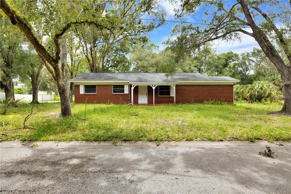 A single-story red brick house sits behind an overgrown lawn under large oak trees — 11916 DAVIS ROAD, TAMPA, FL