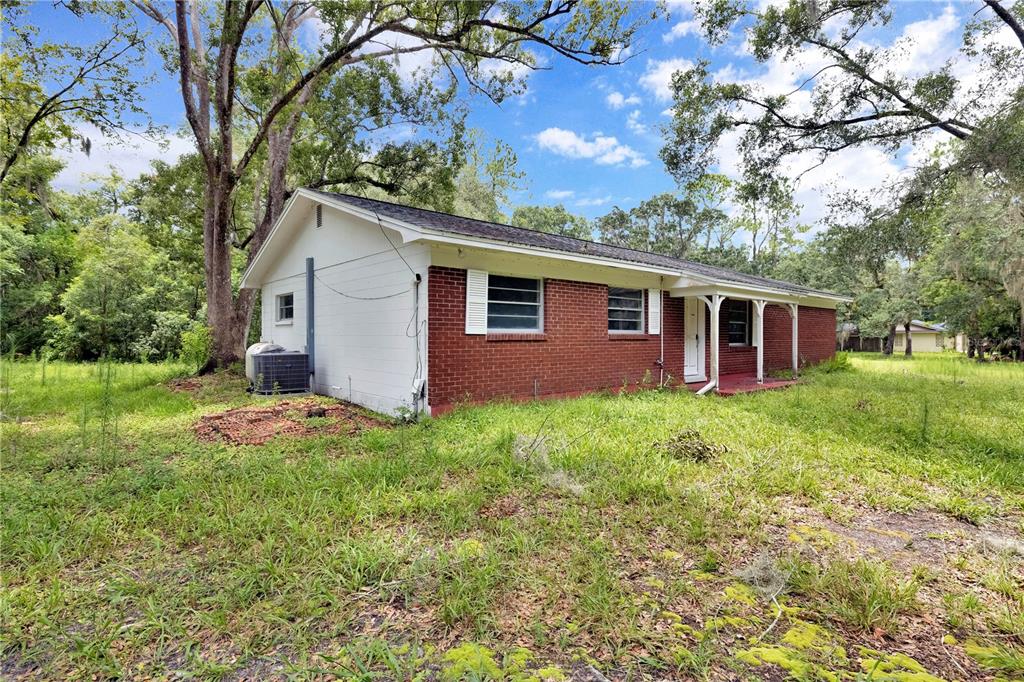 A single-story brick and white-painted house sits on a grassy lot with mature trees — 11916 DAVIS ROAD, TAMPA, FL