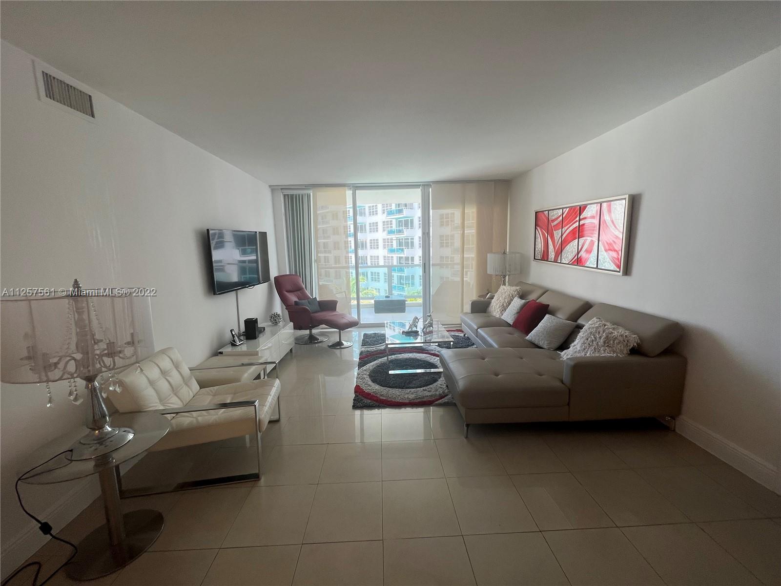 A modern living room features a beige sectional sofa, white armchair, and a balcony view — 5151 Collins Ave # 725, Miami Beach FL 33140, MIAMI BEACH, FL