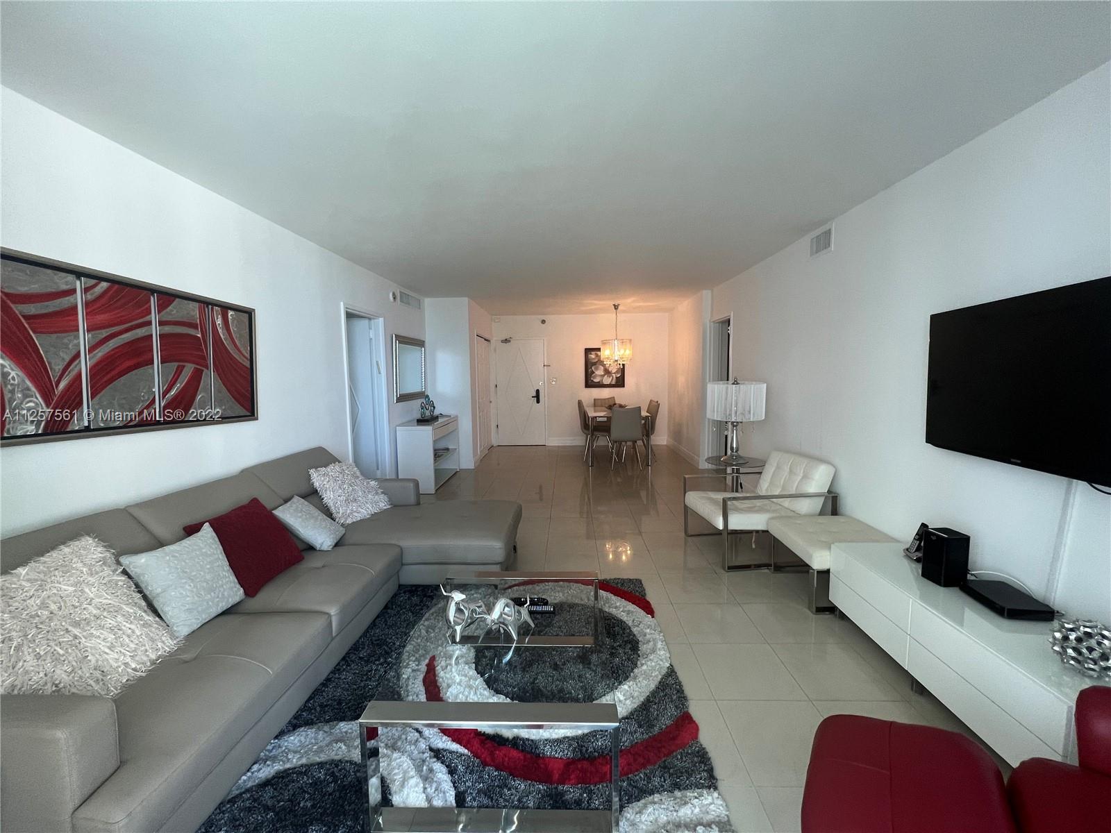 A living room features a grey sectional sofa, a patterned rug, and a wall-mounted television — 5151 Collins Ave # 725, Miami Beach FL 33140, MIAMI BEACH, FL