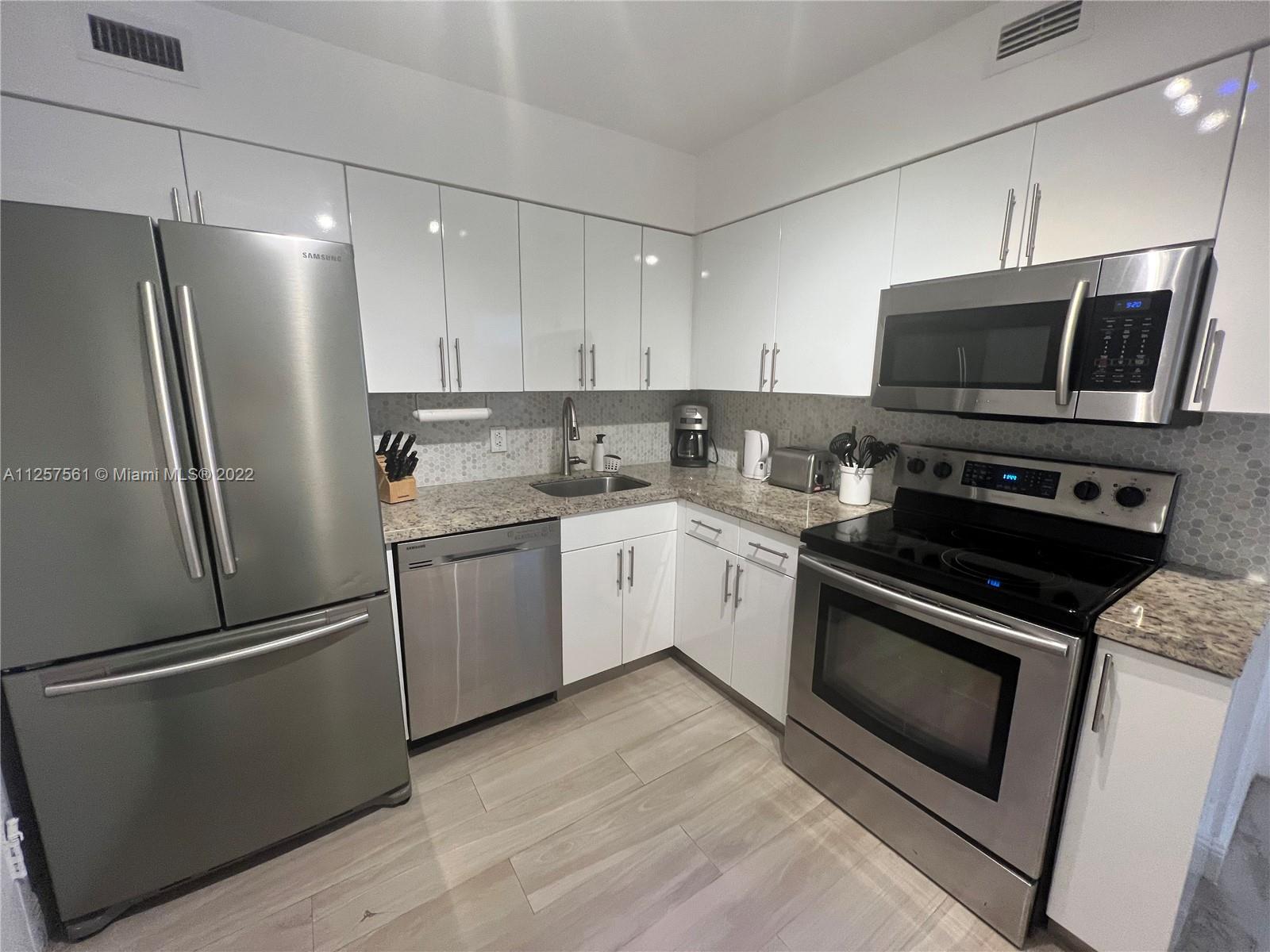 A kitchen features stainless steel appliances, white cabinetry, and a speckled granite countertop — 5151 Collins Ave # 725, Miami Beach FL 33140, MIAMI BEACH, FL