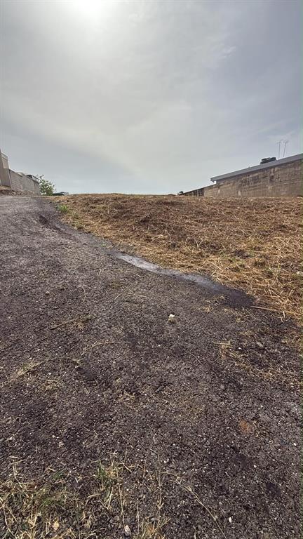 A view of a vacant, sloped dirt lot bordered by a paved path and concrete walls — CARR 637 BO MIRAFLORES SECTOR BIAFARA, ARECIBO, PR