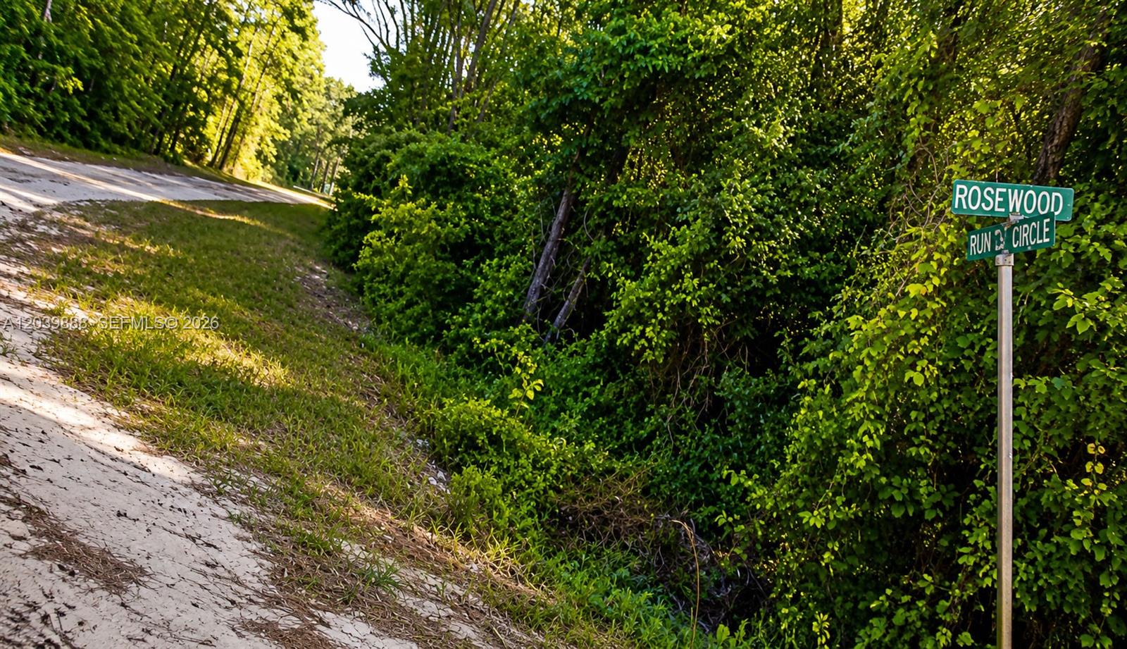 A street sign for Rosewood Run Circle stands beside a dirt road and dense woods — OTHER CITY - IN THE STATE OF FLORIDA, FL