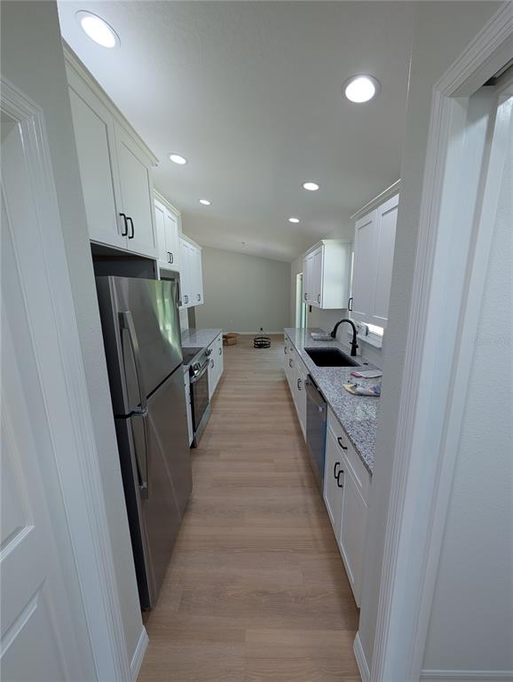 A galley kitchen features white cabinets, granite countertops, stainless steel appliances, and light wood flooring — 4244 SW 157TH COURT SW, OCALA, FL
