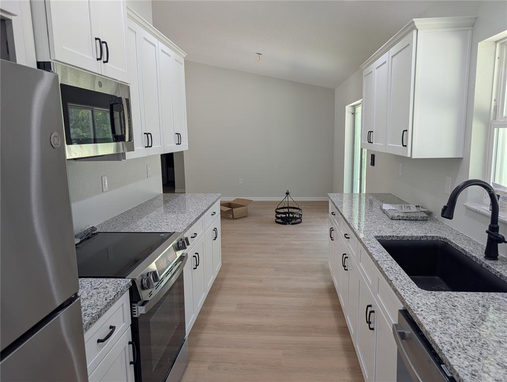 A galley kitchen features white cabinets, granite countertops, stainless steel appliances, and light wood flooring — 4244 SW 157TH COURT SW, OCALA, FL