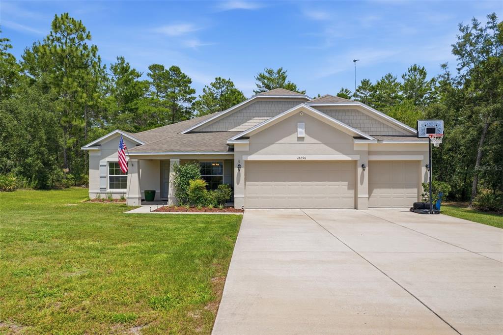 A single-story suburban house with a beige stucco exterior, a three-car garage, and a lawn — 18296 MABERLY ROAD, WEEKI WACHEE, FL