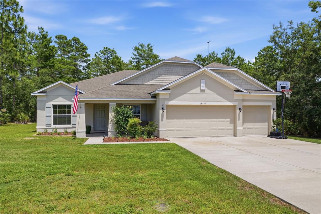 A single-story house with a beige stucco exterior, a three-car garage, and a front lawn — 18296 MABERLY ROAD, WEEKI WACHEE, FL