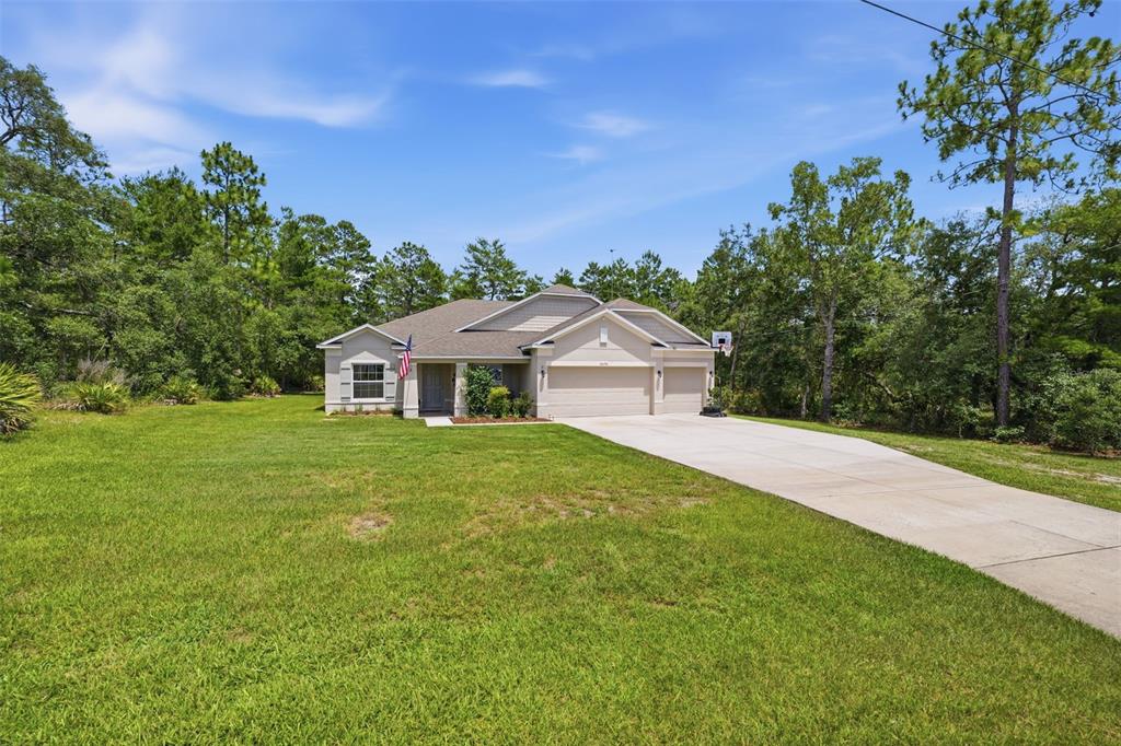 A single-story house with a beige exterior, a concrete driveway, and surrounding trees — 18296 MABERLY ROAD, WEEKI WACHEE, FL