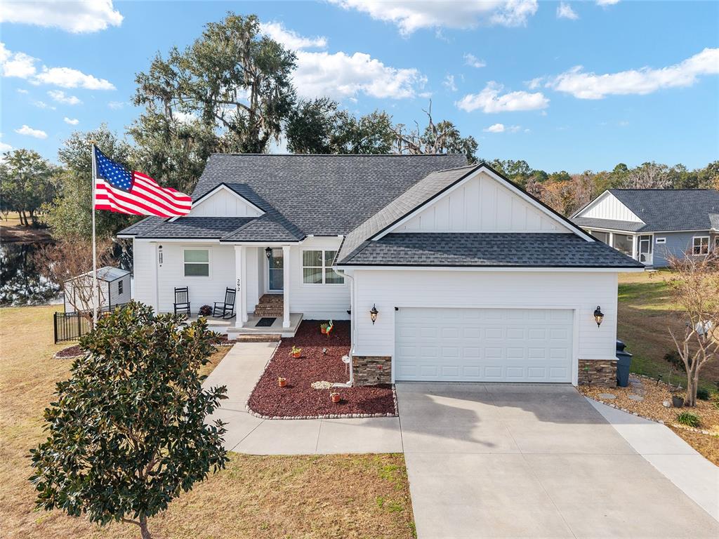 A white house with a dark shingled roof, a two-car garage, and an American flag — 292 SW OLD CYPRESS WAY, LAKE CITY, FL