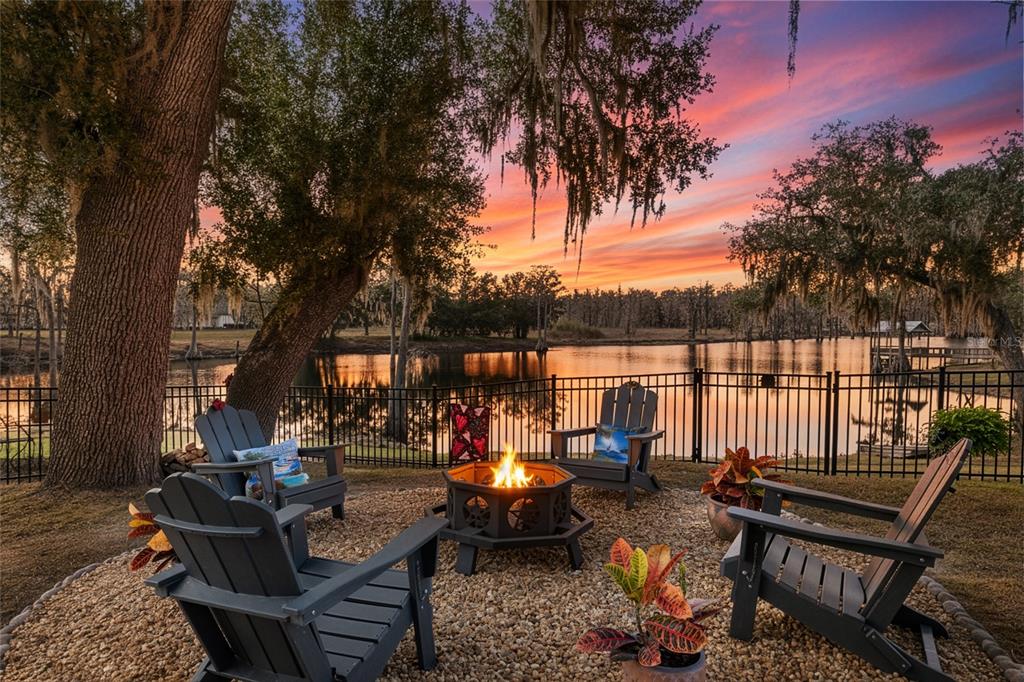 A fire pit with Adirondack chairs sits on a gravel patio overlooking a lake — 292 SW OLD CYPRESS WAY, LAKE CITY, FL