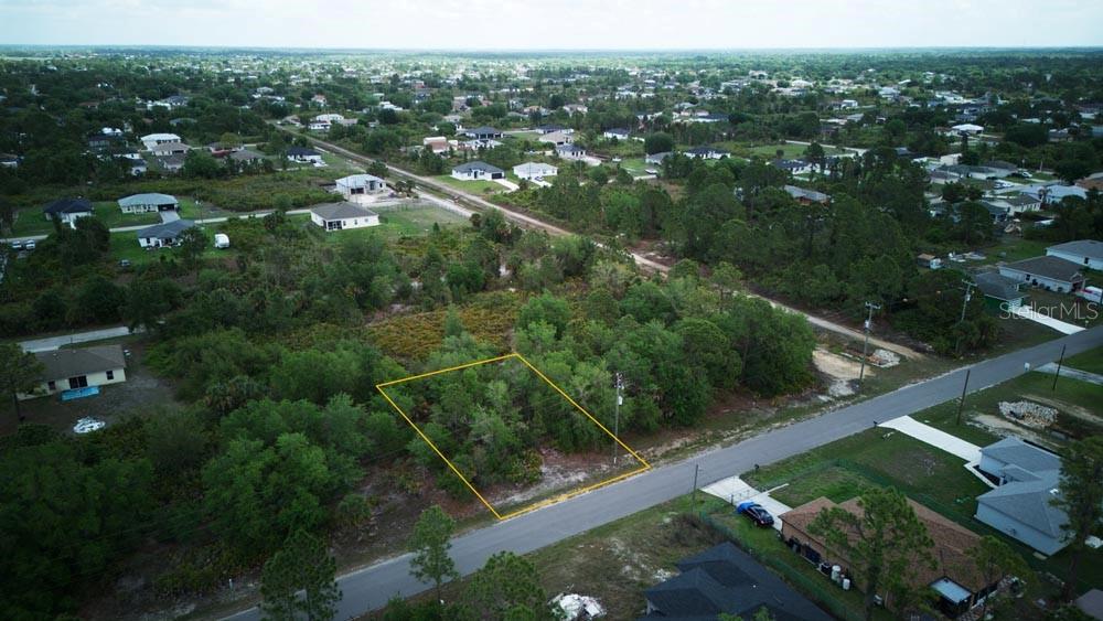 An aerial view shows a vacant, wooded residential lot outlined in yellow along a paved road — 3104 51ST STREET W, LEHIGH ACRES, FL