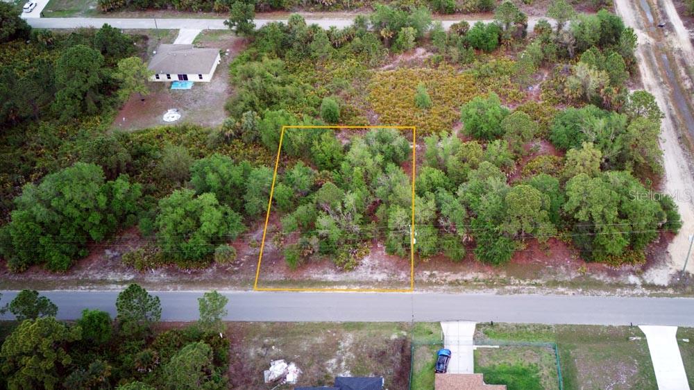 An aerial view shows a rectangular, wooded vacant lot outlined in yellow along a paved road — 3104 51ST STREET W, LEHIGH ACRES, FL