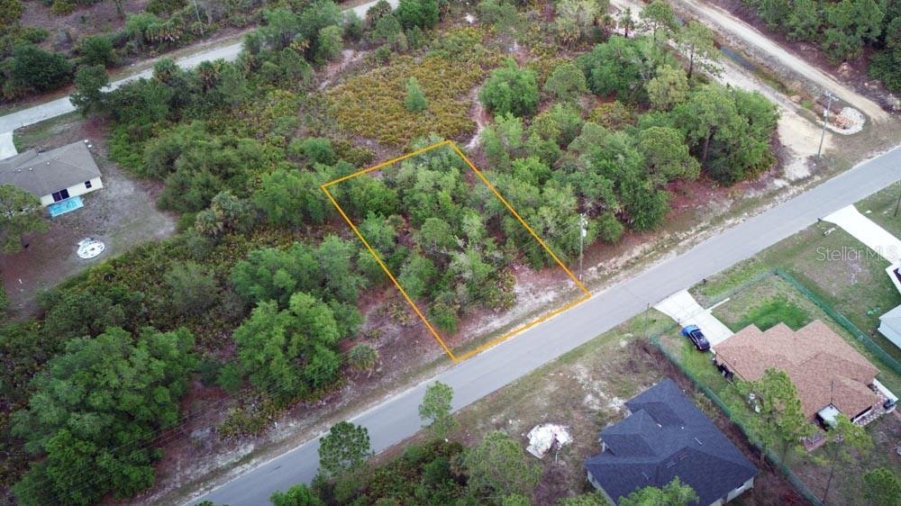 An aerial view shows a rectangular, wooded vacant lot outlined in orange along a road — 3104 51ST STREET W, LEHIGH ACRES, FL