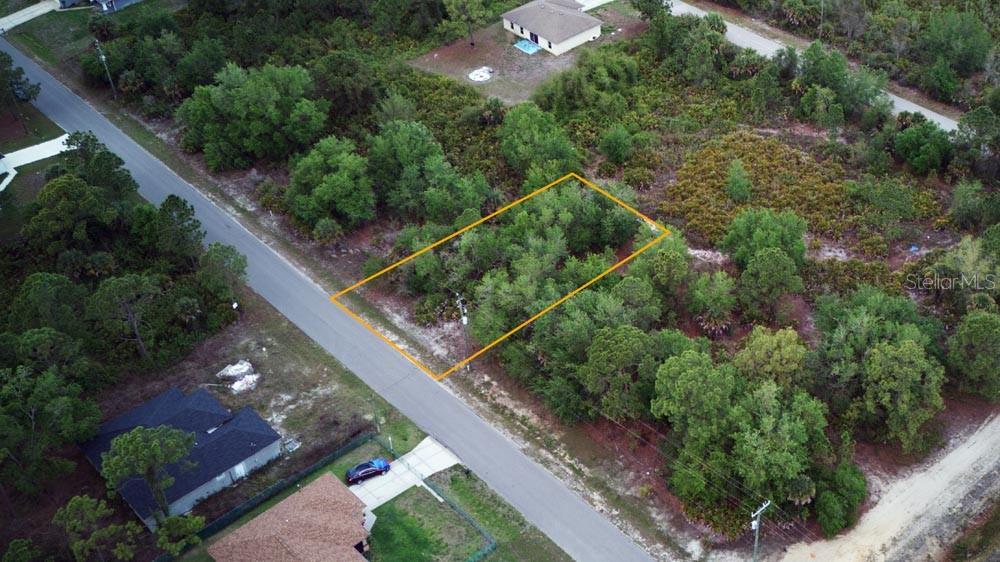 An aerial view shows a rectangular, wooded vacant lot outlined in orange along a road — 3104 51ST STREET W, LEHIGH ACRES, FL