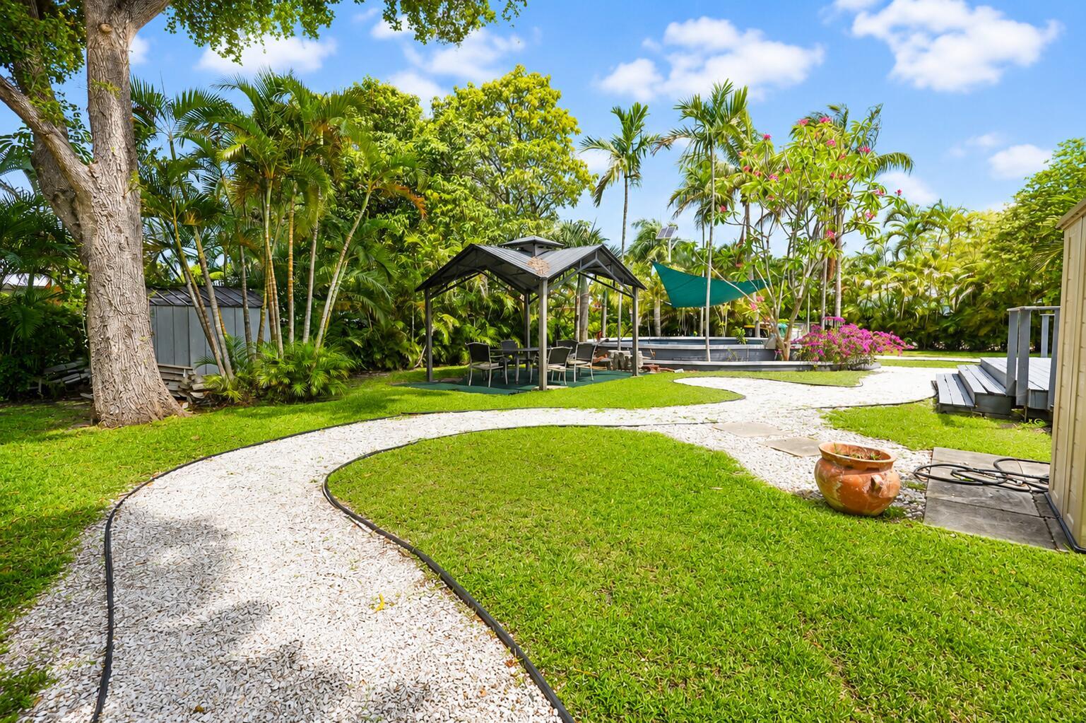 A gravel path winds through a grassy backyard featuring a gazebo, palm trees, and decking — 249 SW 14th Street # 4, Dania Beach FL 33004, DANIA BEACH, FL