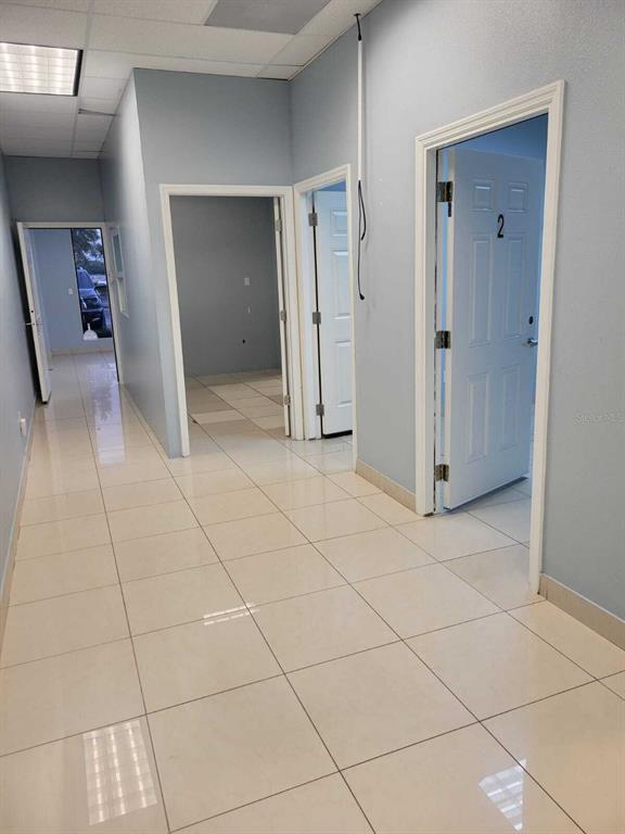 A hallway with light-colored tile flooring leads to multiple doorways in an office space — 1901 S JOHN YOUNG PARKWAY UNIT 103, KISSIMMEE, FL
