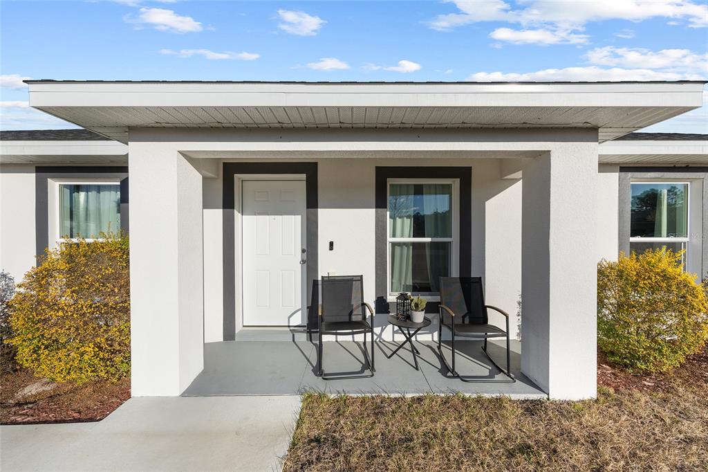 A white house exterior features a covered front porch with two chairs and a table — 3597 SW 151ST AVENUE, OCALA, FL