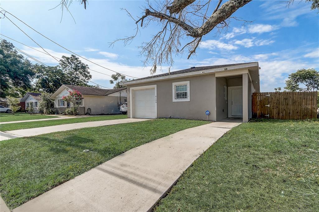 A single-story house with a white garage door, a concrete driveway, and a wooden fence — 6120 DENSON DRIVE, ORLANDO, FL