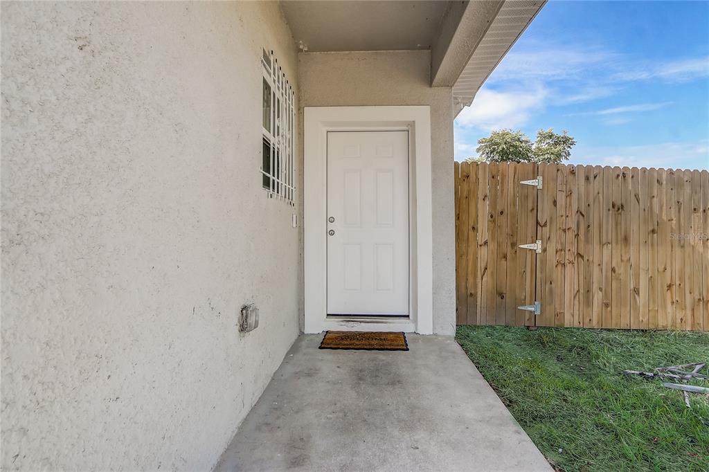 A white exterior door opens onto a concrete patio next to a wooden privacy fence — 6120 DENSON DRIVE, ORLANDO, FL