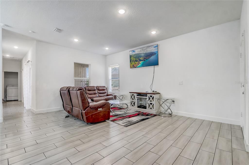 A living room features light tile flooring, a brown leather sofa, and a wall-mounted television — 6120 DENSON DRIVE, ORLANDO, FL