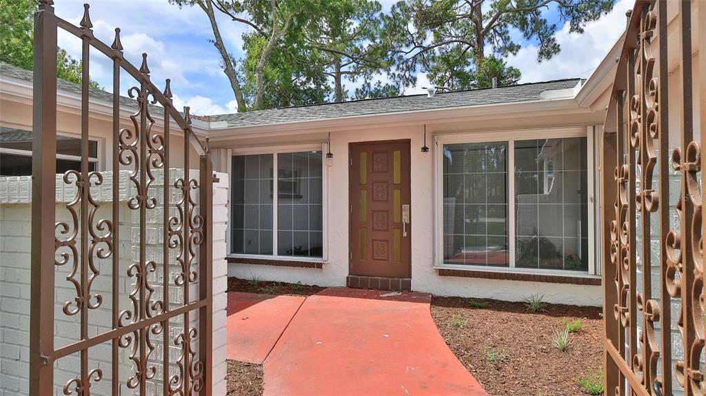 A brown front door is centered between two large windows behind an open metal gate — 2212 WOODLAND DRIVE, EDGEWATER, FL