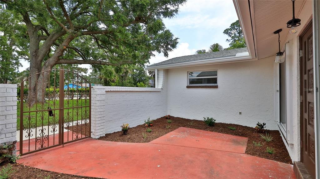 A red concrete patio sits beside a white brick wall and a decorative metal gate — 2212 WOODLAND DRIVE, EDGEWATER, FL