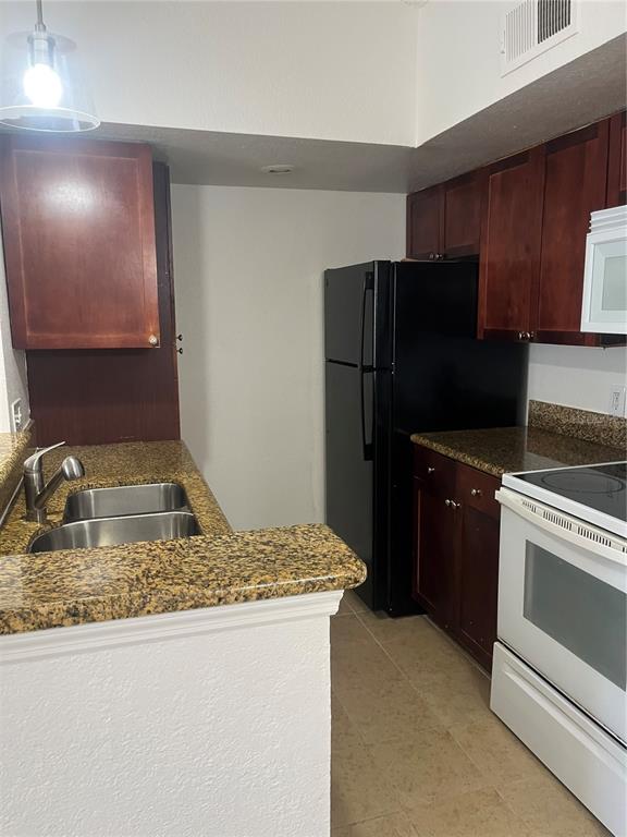 A kitchen features dark wood cabinets, granite countertops, a black refrigerator, and a white stove — 5132 CONROY ROAD UNIT 938, ORLANDO, FL