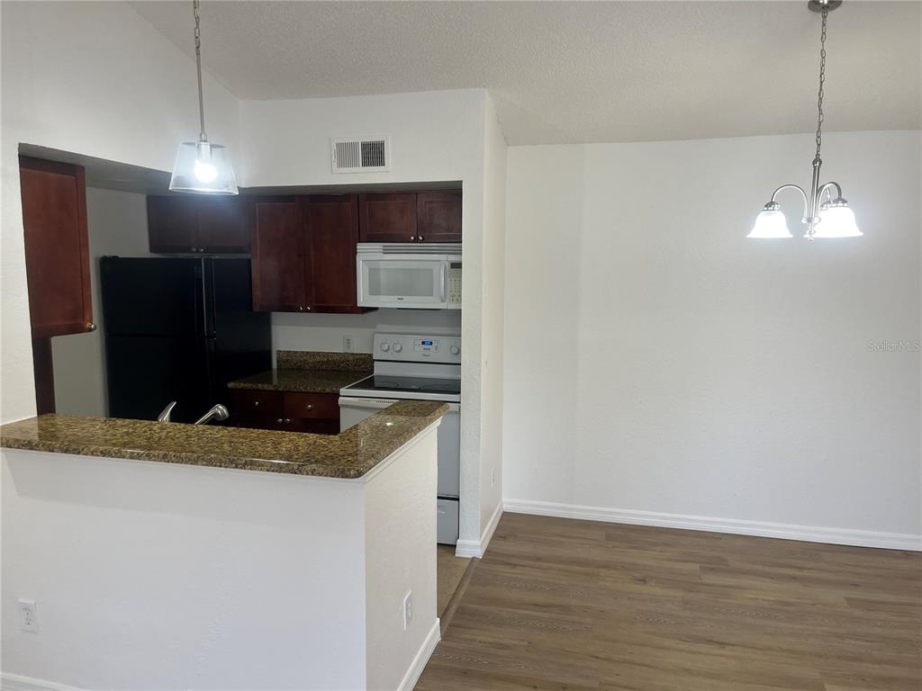 A kitchen with dark wood cabinets, granite countertops, and black appliances overlooks a dining area — 5132 CONROY ROAD UNIT 938, ORLANDO, FL