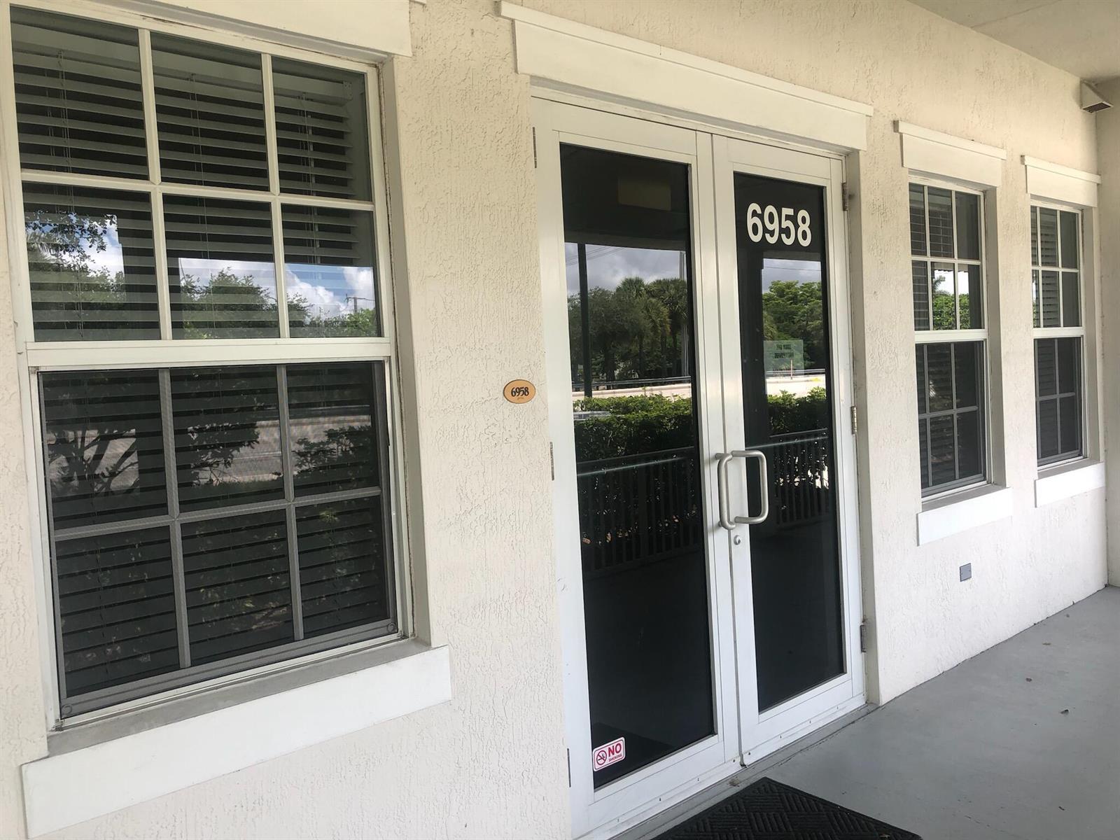 A white building exterior features a double glass door entrance and two windows with blinds — 6958 Griffin Road # 9, Davie FL 33314, DAVIE, FL
