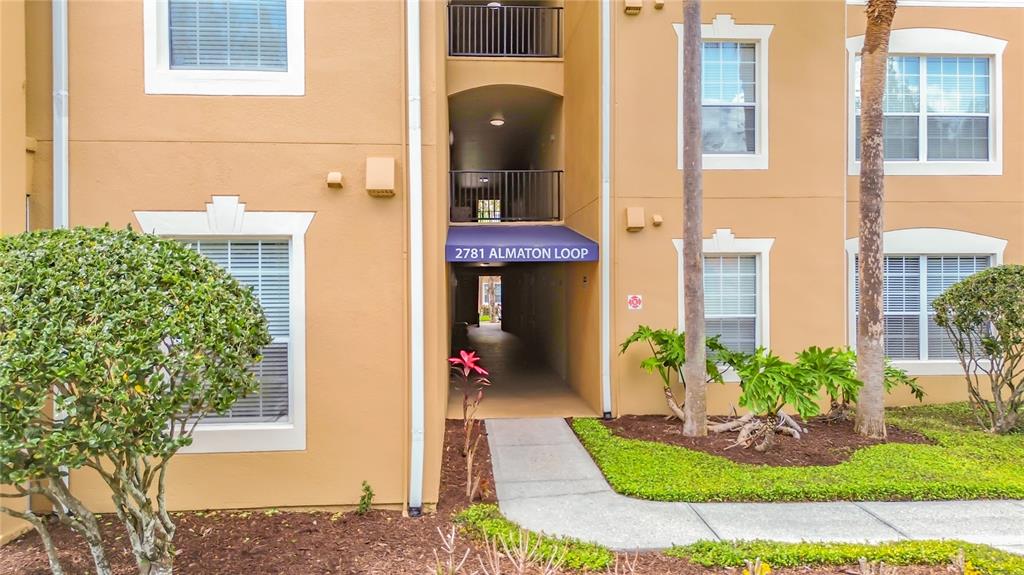 The exterior of a tan apartment building features a covered entryway and landscaped front yard — 2781 ALMATON LOOP UNIT 401, KISSIMMEE, FL