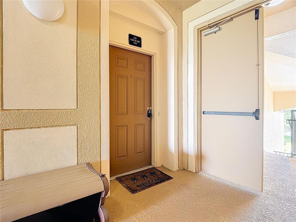 A brown apartment door with a welcome mat is situated in a beige hallway — 2781 ALMATON LOOP UNIT 401, KISSIMMEE, FL