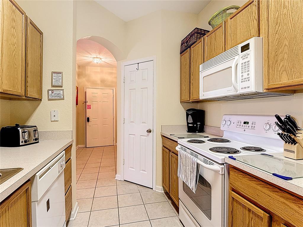 A galley kitchen features light wood cabinets, white appliances, and tiled floors — 2781 ALMATON LOOP UNIT 401, KISSIMMEE, FL