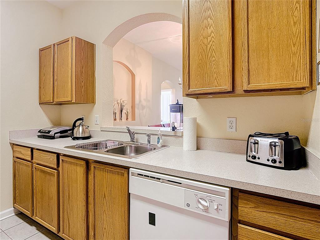 A kitchen features oak cabinets, a double-basin sink, a white dishwasher, and a pass-through window — 2781 ALMATON LOOP UNIT 401, KISSIMMEE, FL